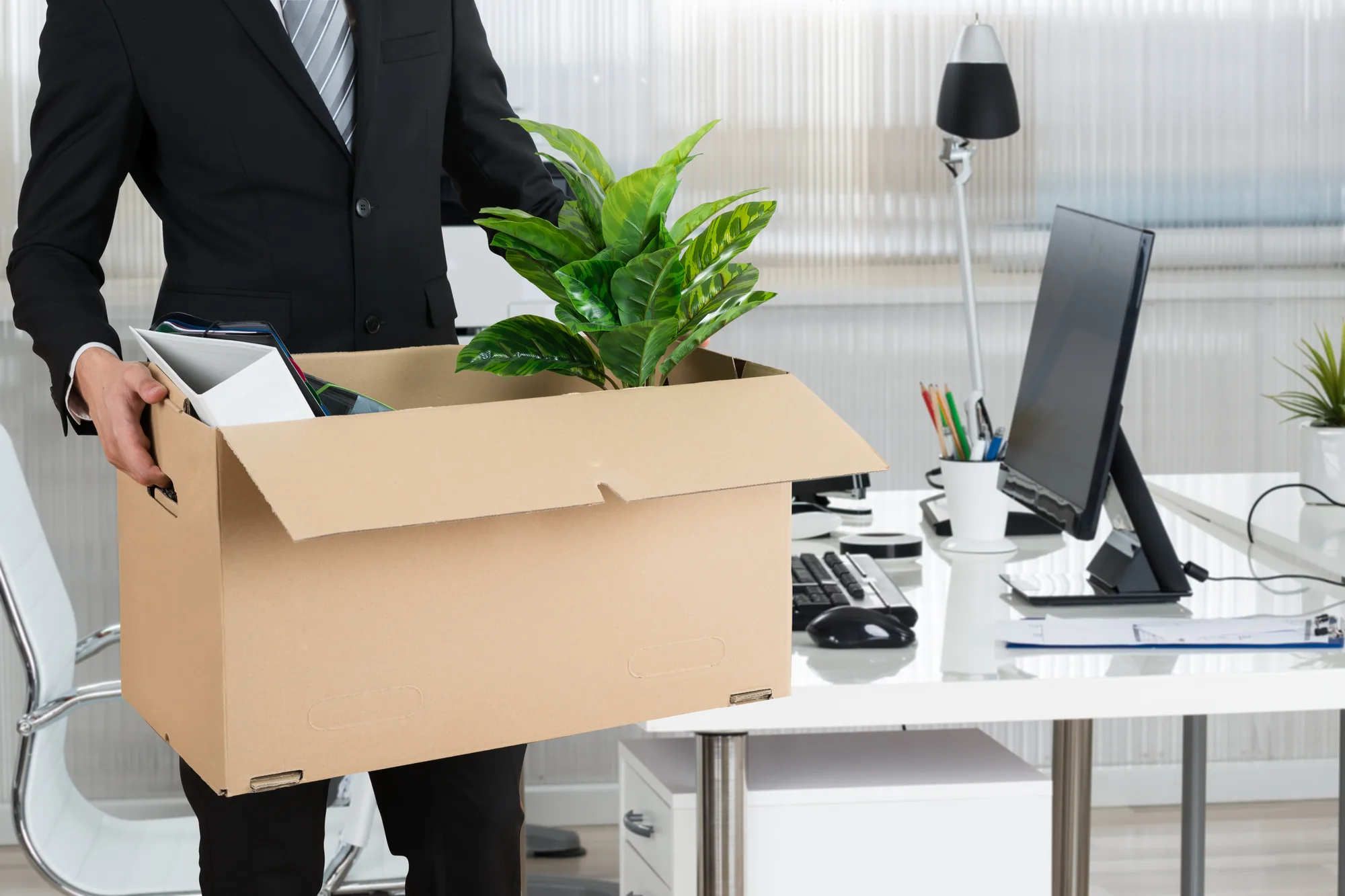 Office worker carrying a box of belongings and a plant from his desk